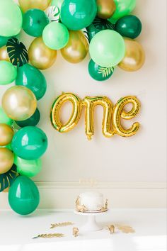 the balloon arch is decorated with gold and green balloons that spell out'one '