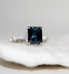 a blue diamond ring sitting on top of a white piece of paper with diamonds around it