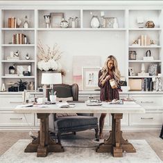 a woman sitting at a desk in front of a white book shelf filled with books