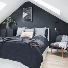 an attic bedroom with black walls and gray bedding, two grey chairs and a painting on the wall