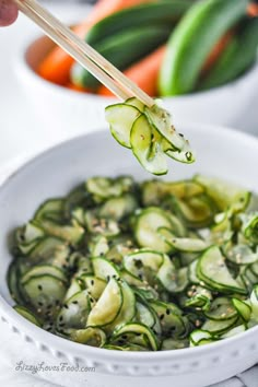 someone holding chopsticks over a bowl of sliced cucumbers