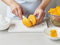 a person cutting up an orange on top of a wooden cutting board next to bowls