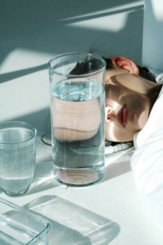 a woman sleeping next to a glass of water and two glasses on a table top