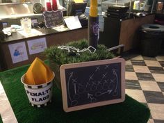 a chalkboard sign sitting on top of a fake grass covered floor next to a potted plant