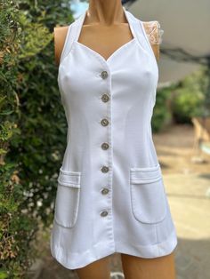 Here is a vintage 1970s white halter polyester tennis dress.Made by Top Seed. Following are the measurements. Bust 32",Waist 28",Hips 38".Made out of a white polyester fabric.Buttons down the front and neck with silver cross buttons. Navy blue top stitching. In nice vintage condition. Please take special consideration of measurements. 1970 sizing was much smaller than today's standards. Take extra special note of length. Tennis dresss were very short not like a regular dress.If you live overseas please email me first before purchasing for mailing cost. Price quoted is for USA only White Lined Halter Neck Mini Dress, Vintage White Mini Dress For Summer, Vintage White Summer Mini Dress, White Halter Neck Mini Dress Lined, White Retro Dress With Buttons, White Halter Neck Lined Mini Dress, White Vintage A-line Mini Dress, White Retro Mini Dress For Summer, Retro White Mini Dress For Summer