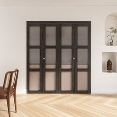 an empty room with a chair and some shelves on the wall behind glass doors that are open