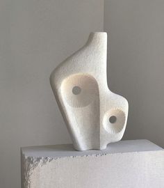 a white sculpture sitting on top of a block of cement in front of a wall