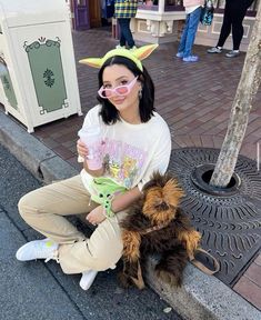 a woman sitting on the curb with her dog wearing yoda mask and drinking from a cup