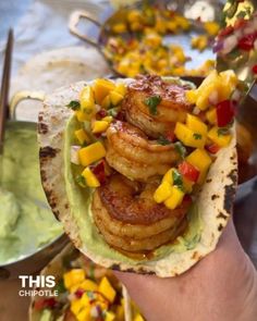 a hand holding a taco filled with shrimp, mango salsa and guacamole