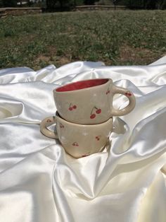 two coffee cups sitting on top of a white cloth covered table with grass in the background