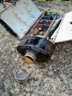 an open box with paint and brushes in it sitting on the ground next to a coin