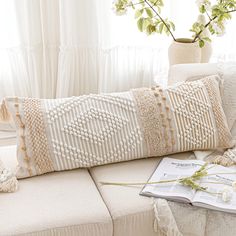 a white couch sitting next to a window with a book on top of it and a potted plant in the corner