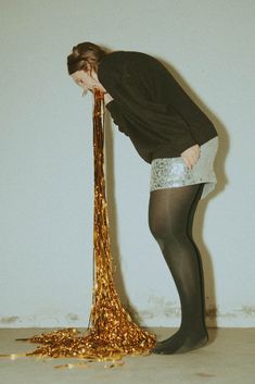 a woman standing next to a tall golden object with her head in the floor and hands behind her back