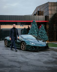 a man standing next to a green sports car in front of a building with christmas trees