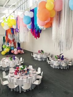 a room filled with tables and chairs covered in white tablecloths, balloons and streamers