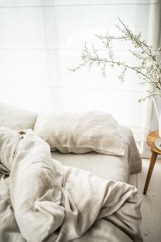 an unmade bed with white linens and flowers in a vase next to it