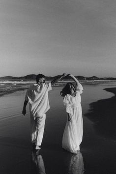 black and white photograph of two people walking on the beach with their arms in the air