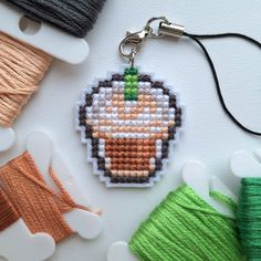 a cross stitch pumpkin keychain with spools of thread next to it