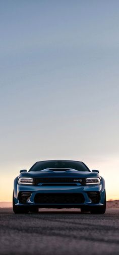 the front end of a blue sports car driving on a road at sunset or dawn