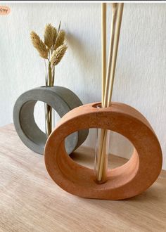 two vases with sticks sticking out of them on a table next to each other