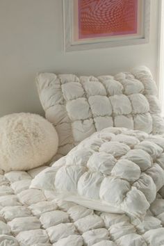 a bed with white comforter and pillows on it next to a framed art piece