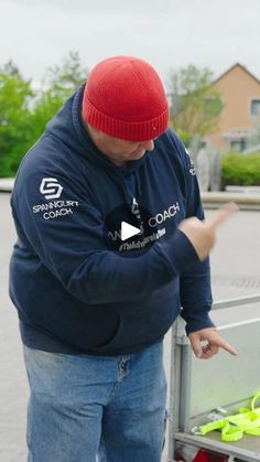 a man in a red beanie points at something while standing next to a cart