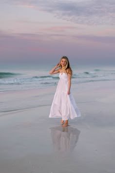 a woman in a white dress standing on the beach