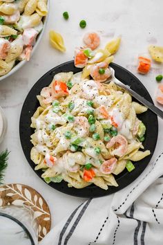 pasta salad with shrimp and peas on a black plate next to a bowl of vegetables