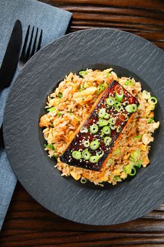 a black plate topped with rice and meat next to a fork on a wooden table