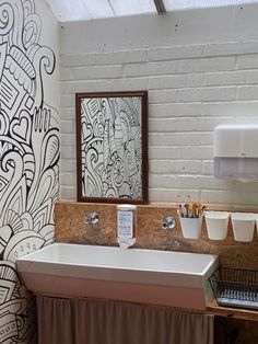 a white sink sitting under a bathroom mirror next to a wall with graffiti on it