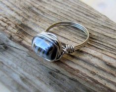 a silver ring sitting on top of a piece of drift wood with a black and white striped glass bead around it