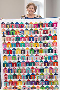 a woman holding up a quilt made with houses