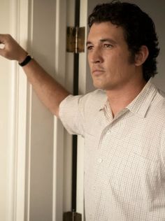 a man in a white shirt is holding on to a door handle and looking at the camera