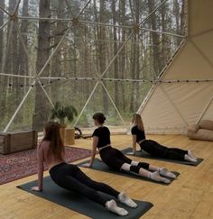 three women are doing yoga in front of a large glass wall with trees behind them