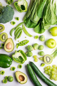 many different vegetables are arranged on a white surface with green leaves and cucumbers