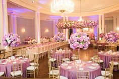 a banquet hall with tables and chairs covered in purple linens, pink flowers and chandeliers