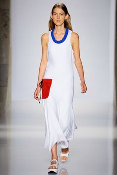 a woman walking down a runway wearing a white dress with red accents on the side