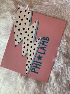 a pink book with polka dots and a lightning bolt on the cover is laying on a fluffy white surface