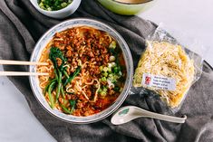 a bowl of noodles and vegetables with chopsticks next to it on a towel