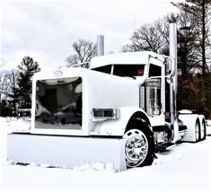 a large white semi truck parked on top of a snow covered field with trees in the background