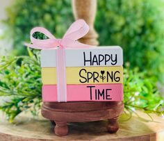 a gift wrapped in pink and yellow paper sitting on top of a wooden stand with the words happy spring time written on it