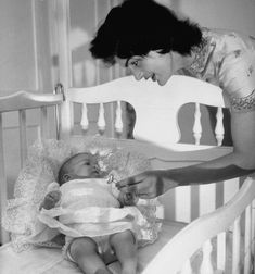 an old photo of a baby in a crib being fed by a woman who is feeding it