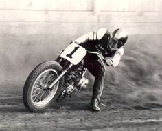 a man riding on the back of a motorcycle down a dirt road next to a wall