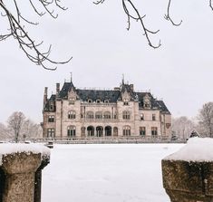 a large stone building sitting on top of a snow covered field in front of trees