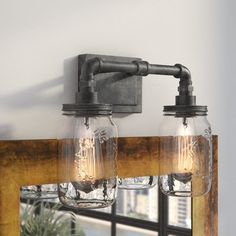 two mason jar lights are hanging on the wall next to a mirror and potted plant