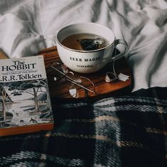 a bowl of soup and glasses on a bed with a book about the hobbit