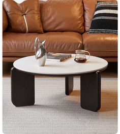 a coffee table with some books and a silver tea pot on it in front of a brown leather couch