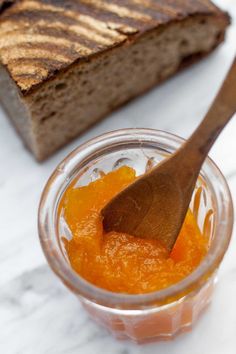 a wooden spoon sitting in a jar filled with orange marmalade jam next to a slice of bread