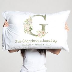 a woman holding up a pillow with the letter g on it and flowers in front of her face