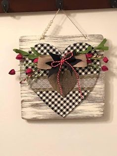 a wooden heart hanging on a wall with flowers and burlocks attached to it